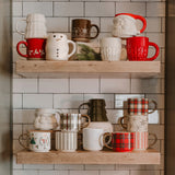 Holiday greenery coffee mug displayed on wooden shelf with festive Christmas mugs and decorations