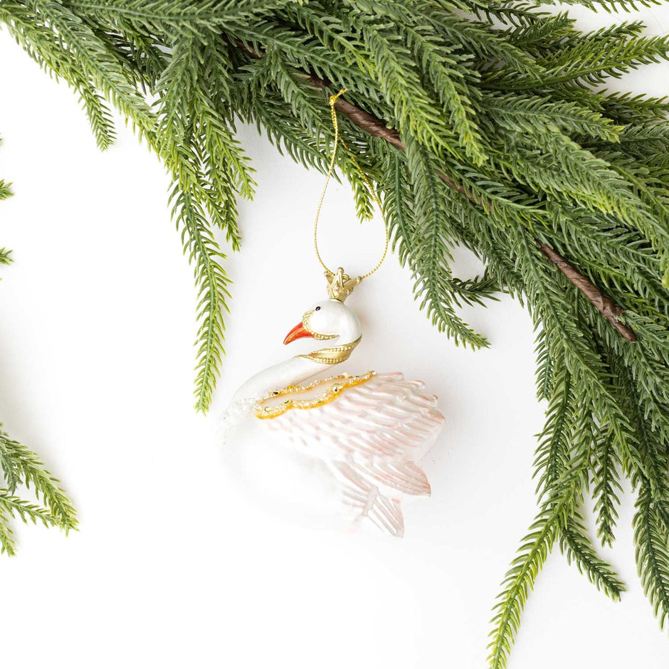 White glass swan ornament with gold accents hanging from evergreen branches