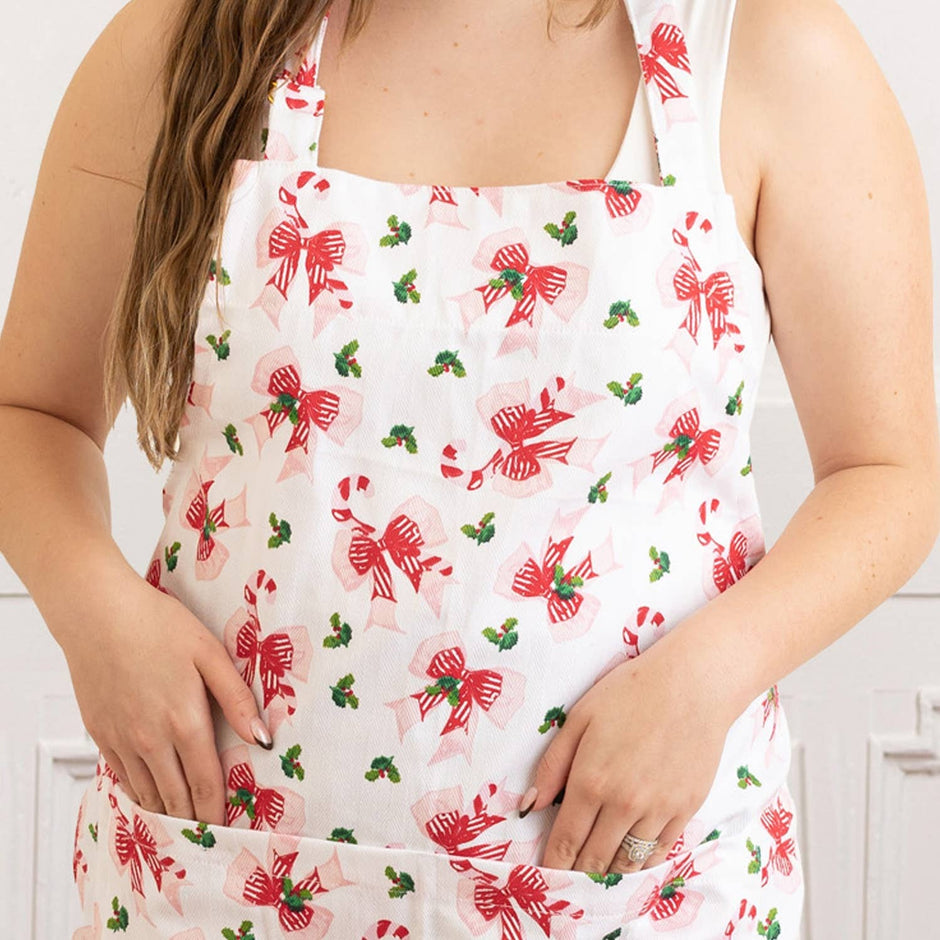 Woman wearing Holly Jolly Bows Apron with red bows and holly pattern on white background
