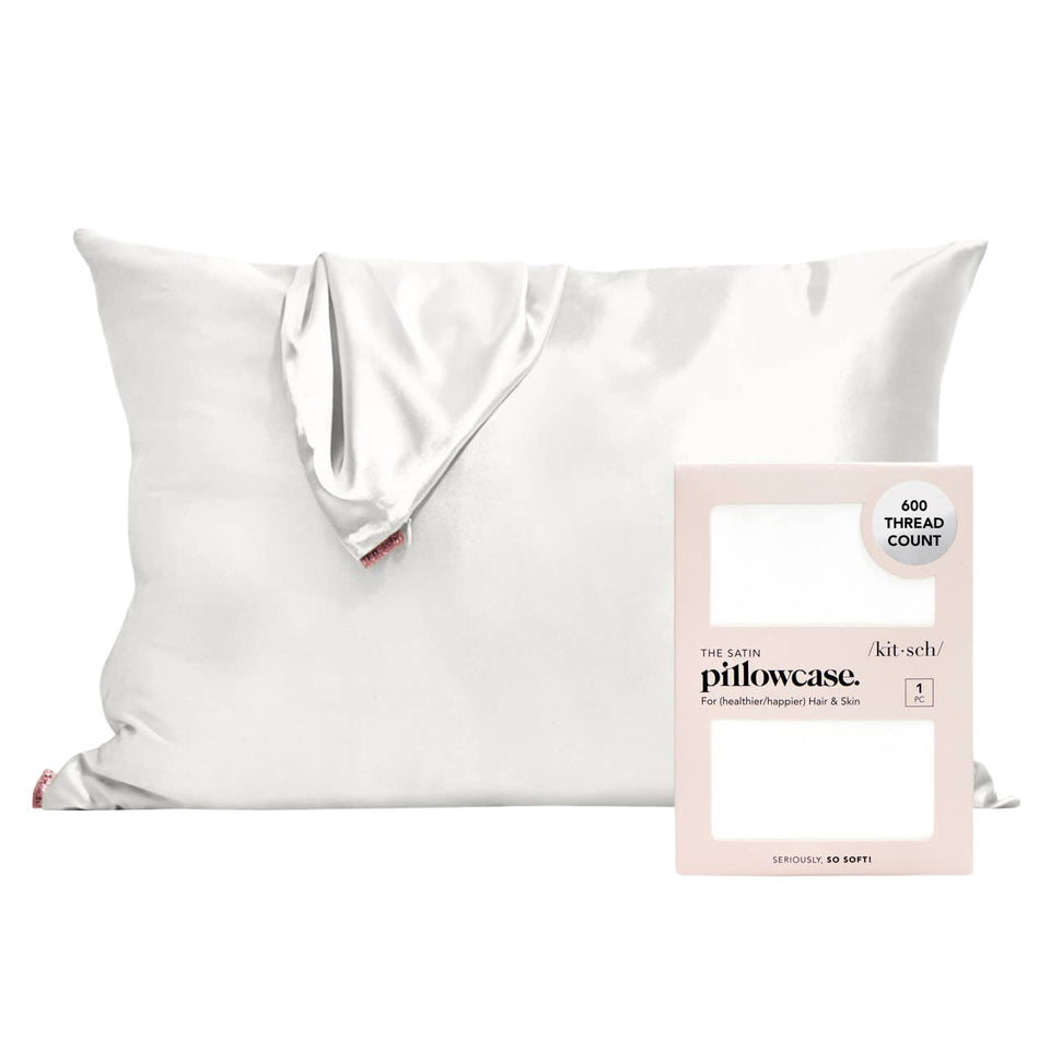 A white satin pillowcase draped over a white pillow, shown next to its light pink retail box labeled 'the pure pillowcase. kit-sch.