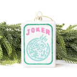 Joker mahjong tile ornament displayed with evergreen branches against white background