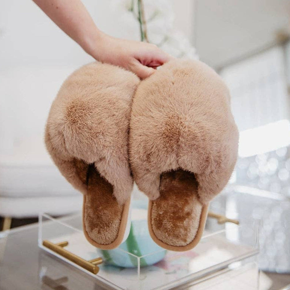 Woman holding tan faux fur jumbo slippers in bright bathroom setting