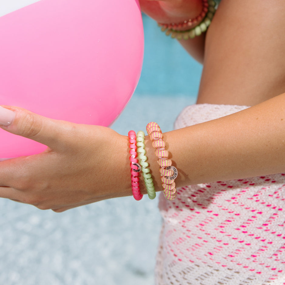 Woman wearing colorful beaded hair ties on wrist holding pink balloon at beach