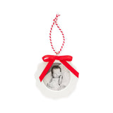 White circular Christmas ornament with red ribbon bow and candy cane string, displaying black and white photo of sleeping newborn