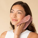 Woman using pink microfiber face towel for skincare routine on neutral background