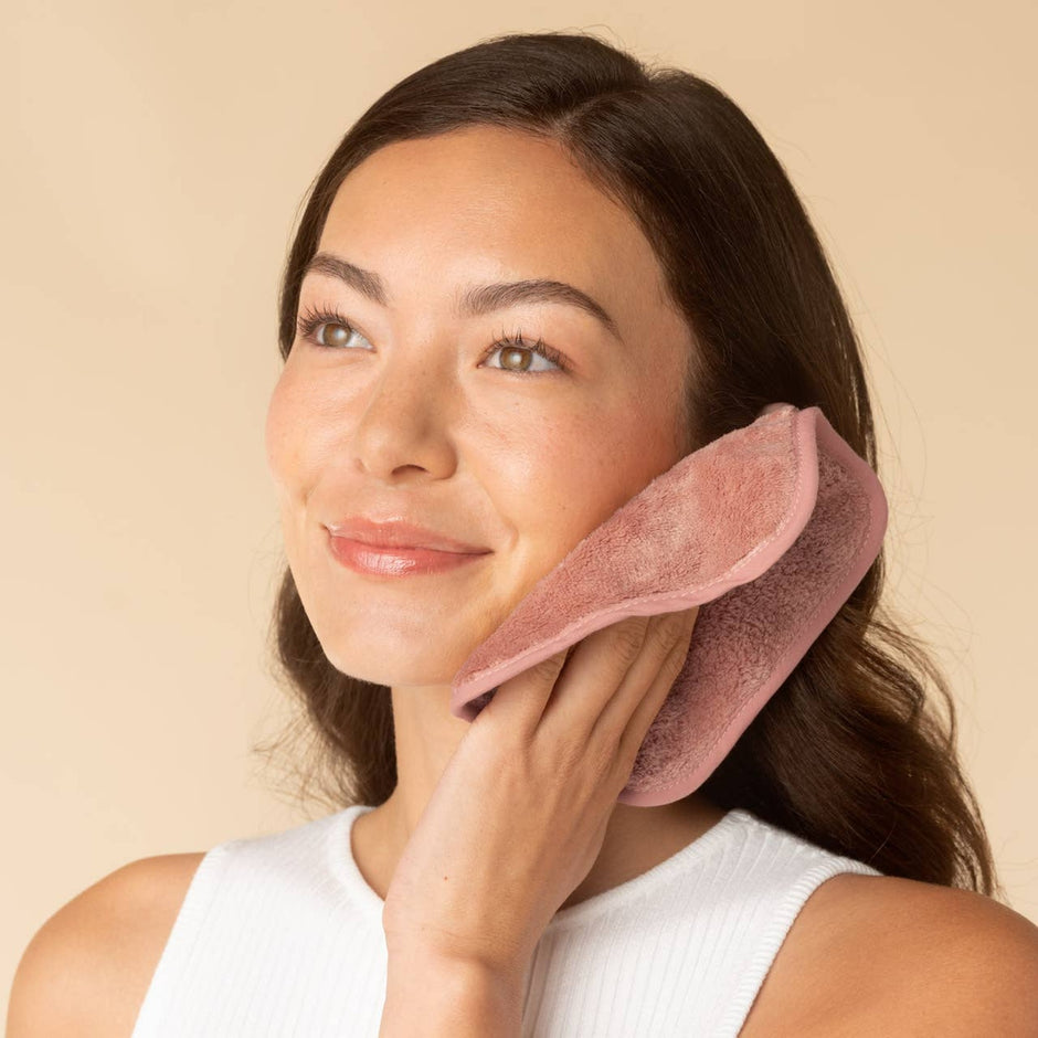 Woman using pink microfiber face towel for skincare routine on neutral background