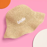 Beige straw bucket hat with white 'bride' embroidery on pink background