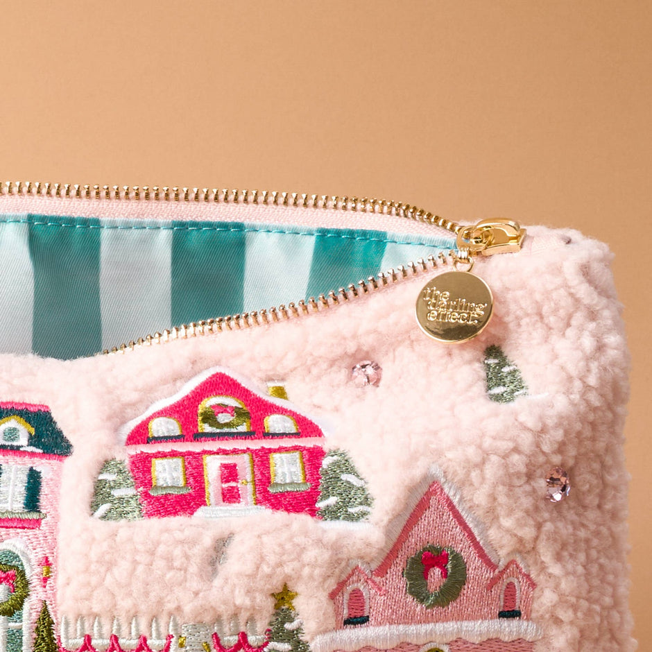 Pink teddy pouch with embroidered holiday village houses, gold zipper and charm detail