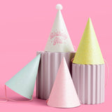Pastel glitter paper party hats in white, pink, mint, and yellow with pom-pom toppers