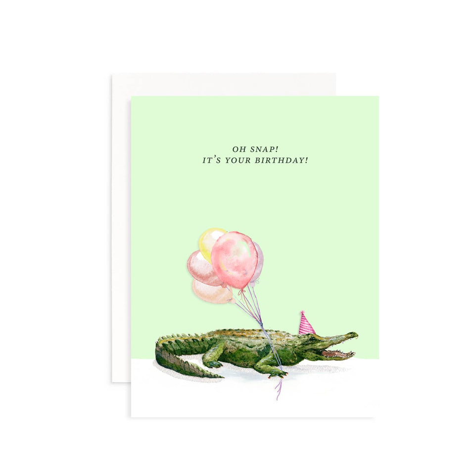 Birthday card with a crocodile holding balloons and a party hat on a light green background.