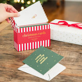 Hand holding open a red and white striped Christmas card box with assorted festive cards displayed