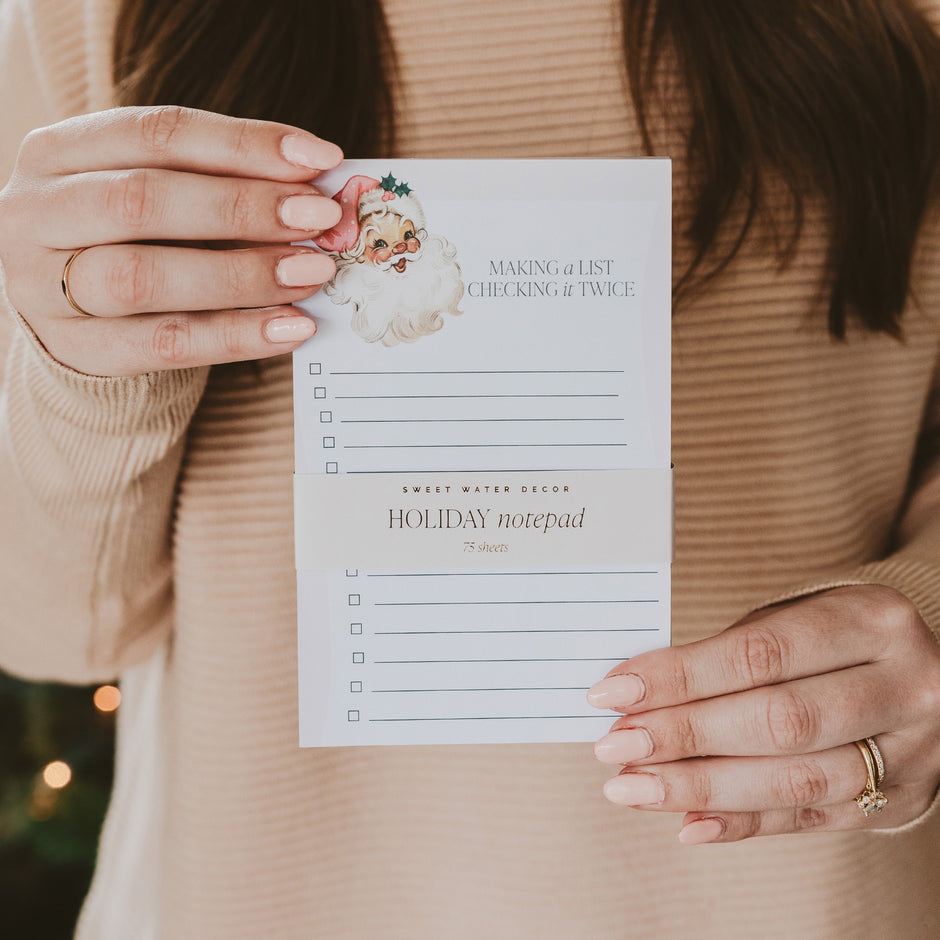 Woman holding Sweet Water Decor vintage Santa holiday notepad with checkboxes and festive design