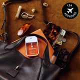 Touchland hand sanitizer displayed in a styled flat lay with accessories, wallet, and cosmetics on brown fabric.