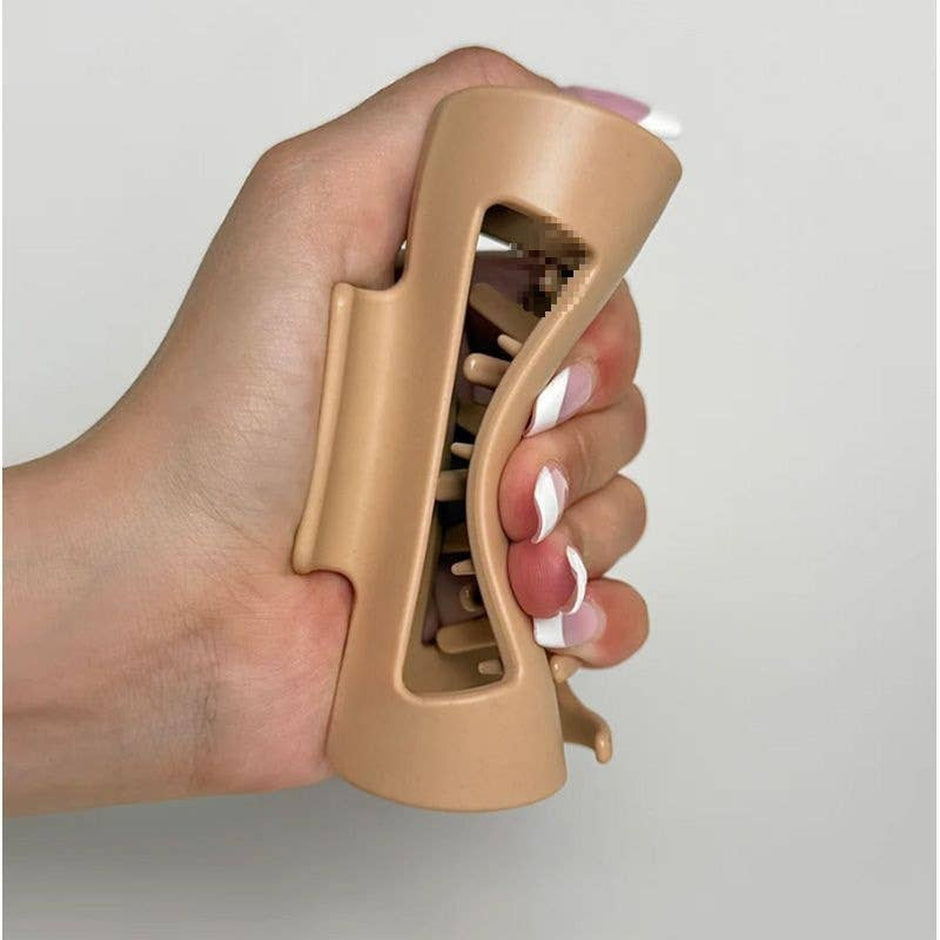 Beige minimalist claw clip held in hand with manicured nails against neutral background