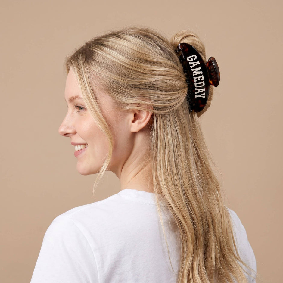 Woman wearing black tortoiseshell claw clip with 'Gameday' text in long blonde hair
