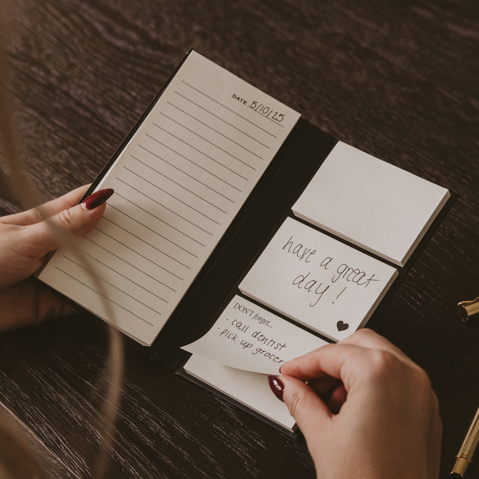 Hands holding open portable sticky notes booklet with date and to-do list reminders