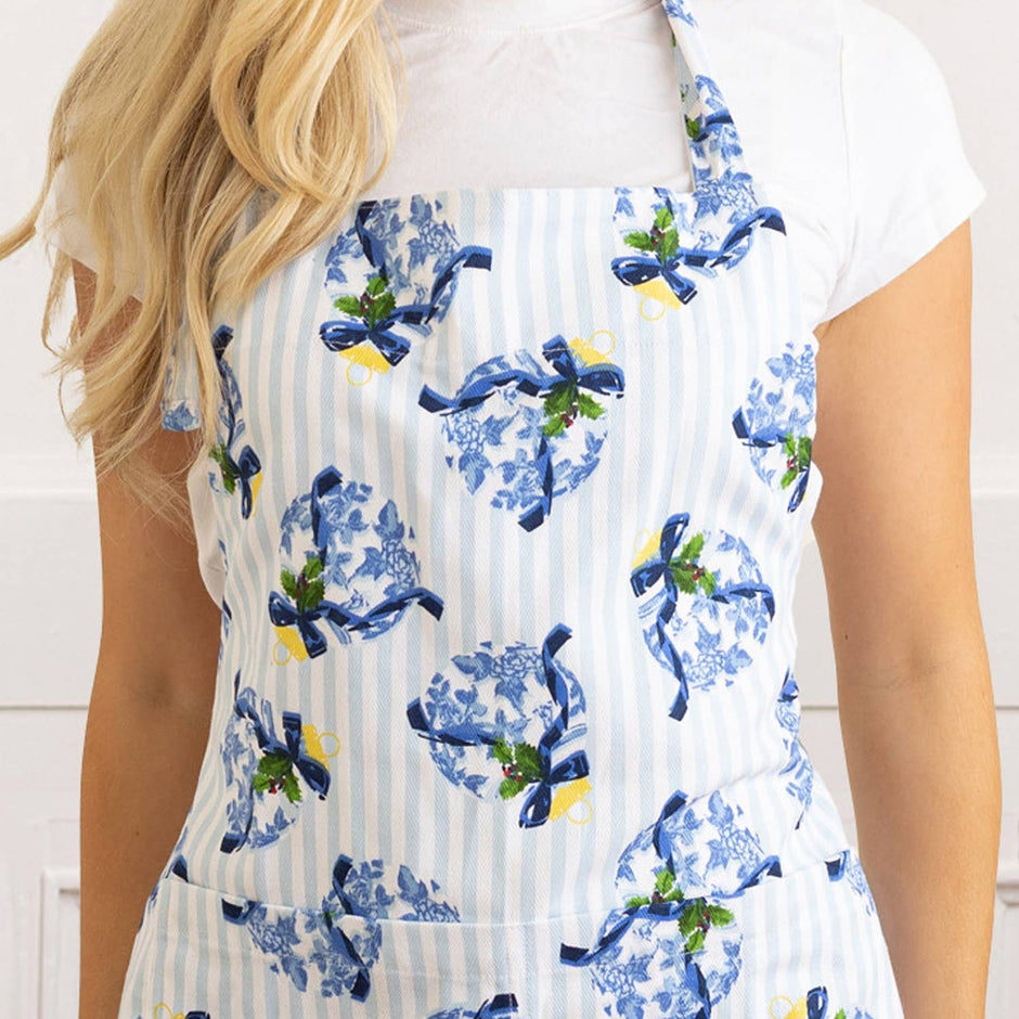 Woman wearing white Holiday Chinoiserie apron with blue floral bow pattern and green herb details