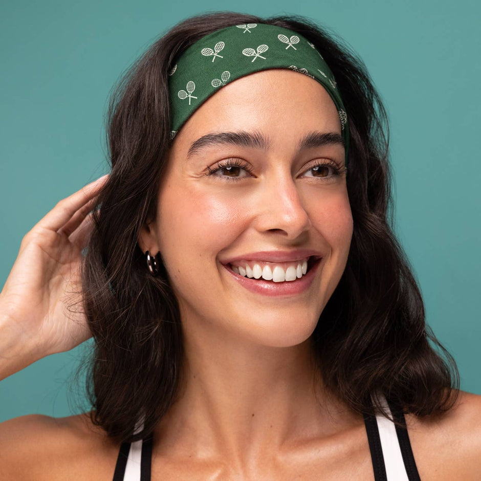 Woman wearing green tennis-patterned headband against turquoise background, smiling