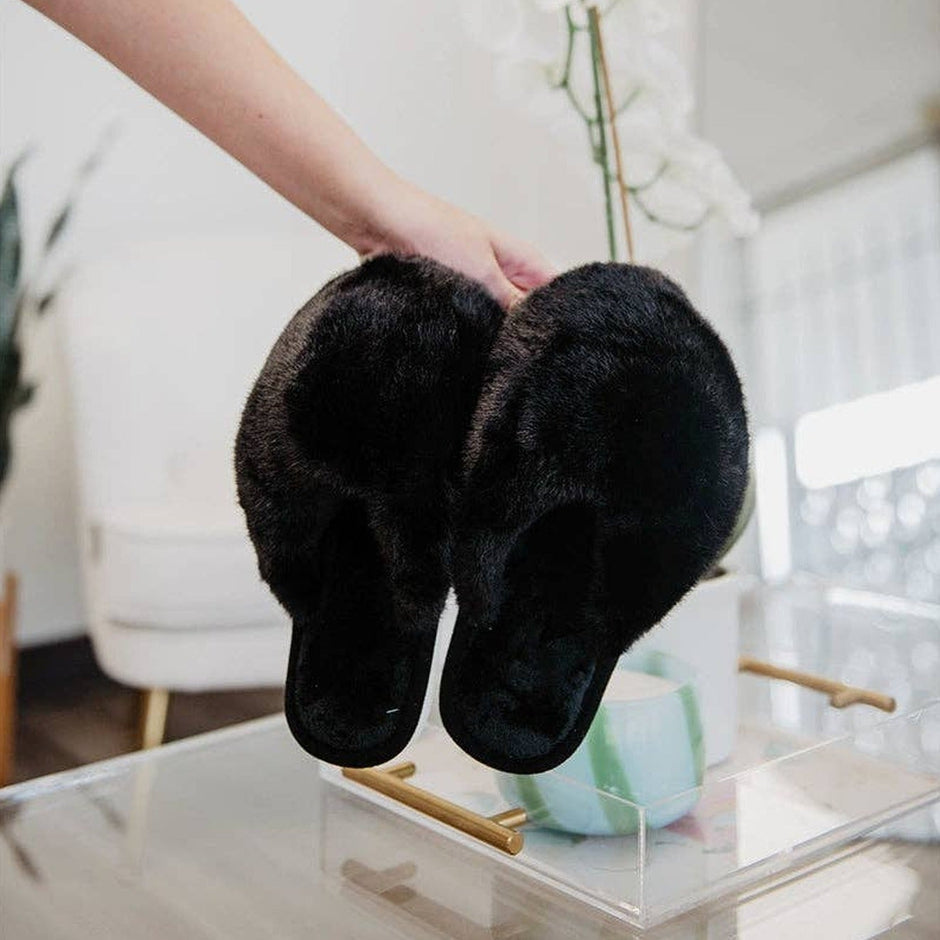 Woman wearing black faux fur jumbo slippers in bright modern bedroom with plants
