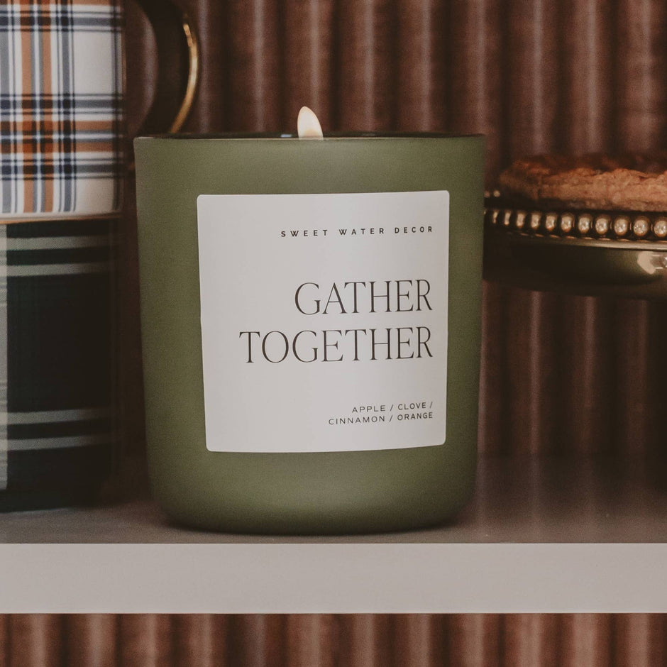 Gather Together soy candle by Sweet Water Decor displayed on shelf with fall decor and books