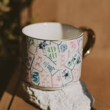 Mahjong Tiles Coffee Mug held in hand, showing colorful tile pattern design with brass handle
