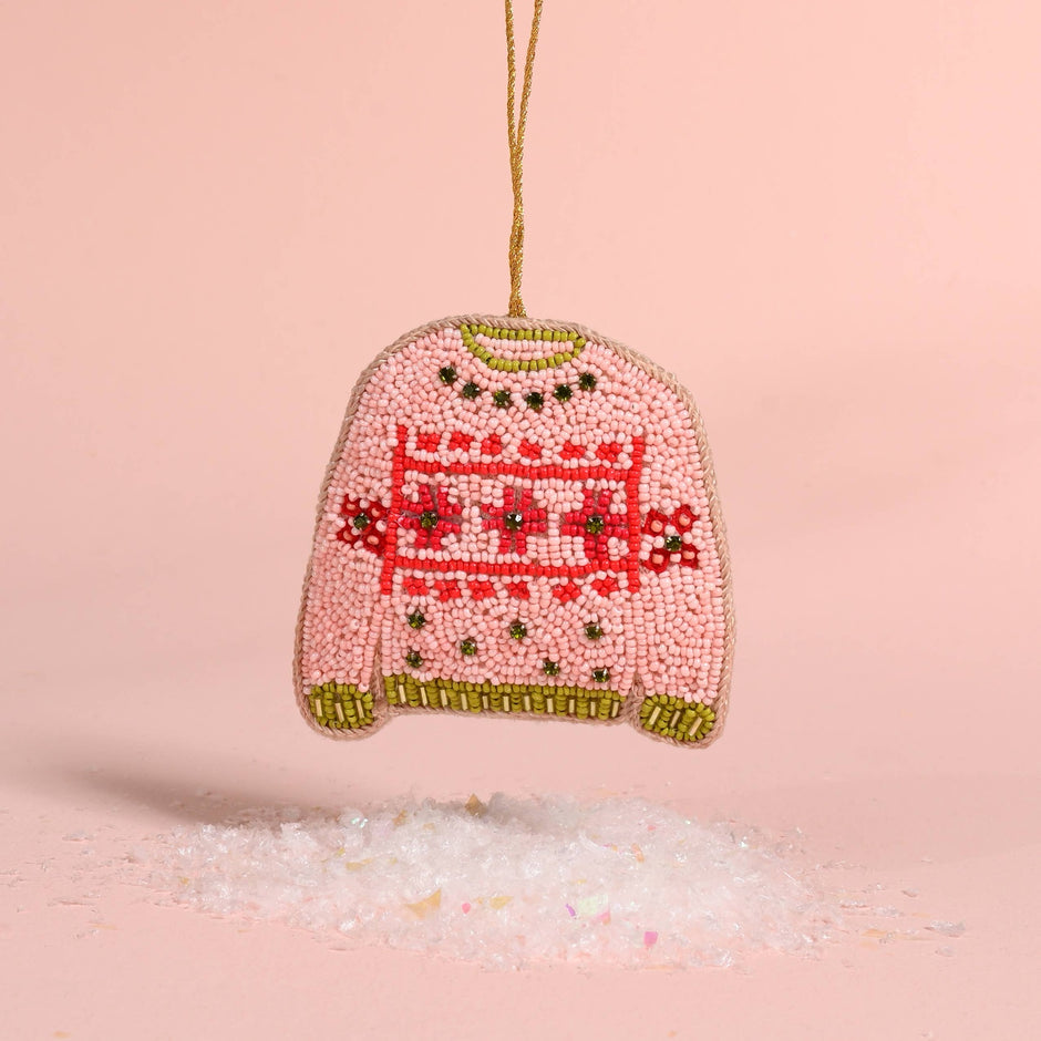 Pink beaded Christmas sweater ornament with red pattern and gold trim, hanging against pink background