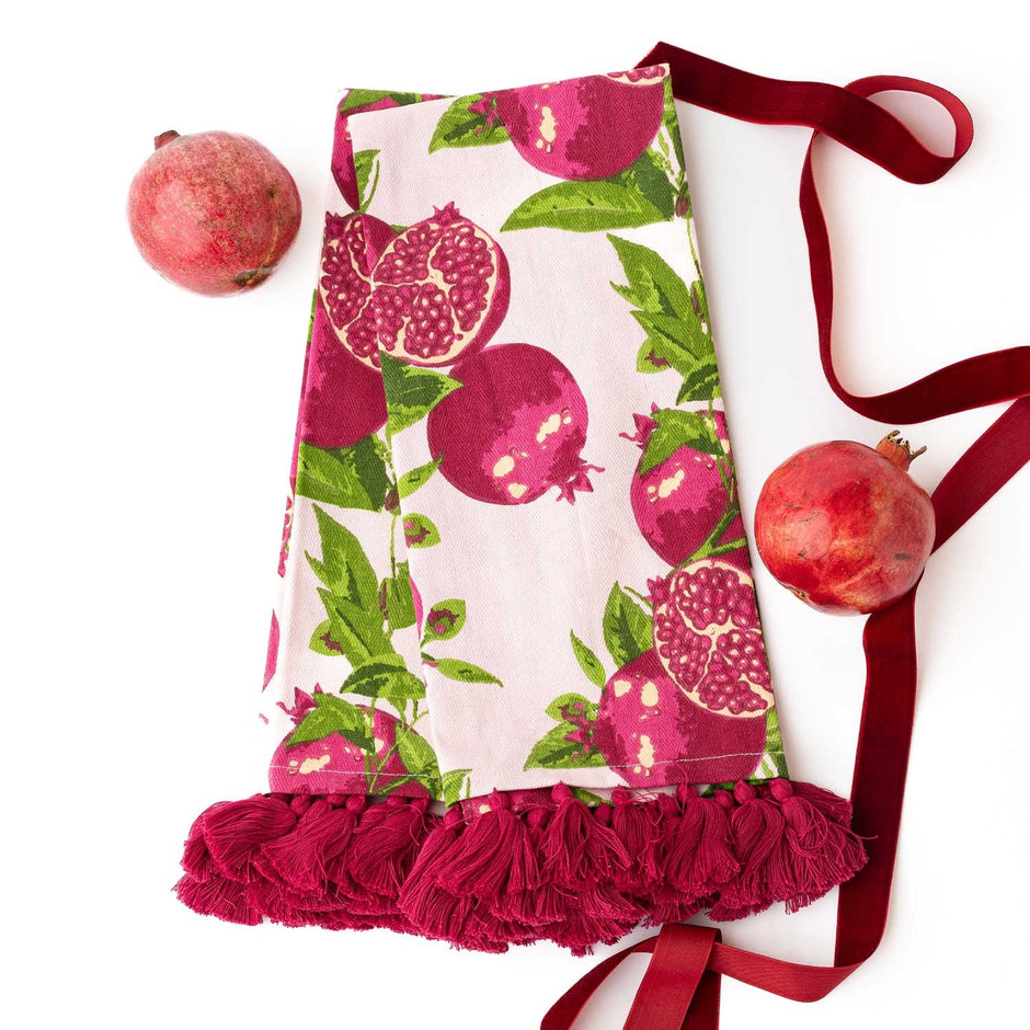 Pomegranate Grove kitchen towel with tassel trim displayed with fresh pomegranates and burgundy ribbon
