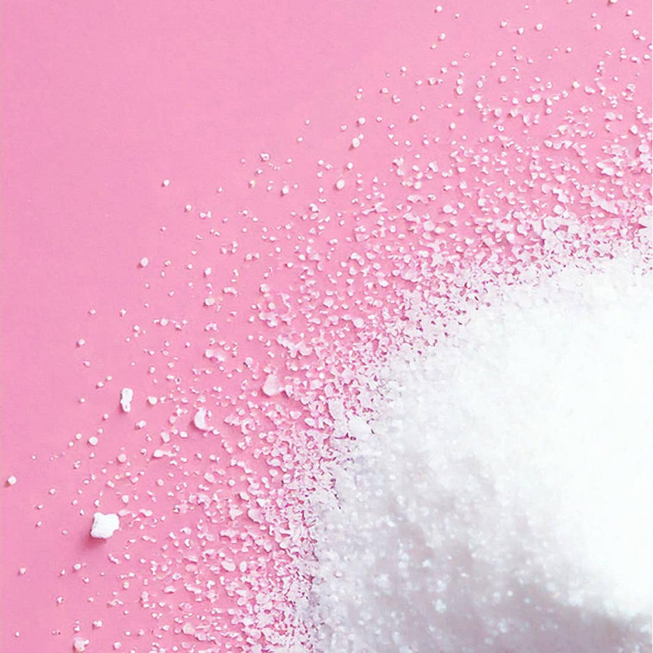 White bath soak crystals scattered on pink background, creating gradient transition effect