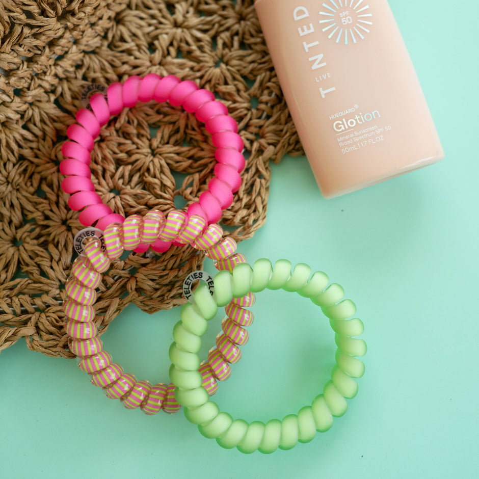 TELETIES Summer Crush Large Hair Ties in pink and green with Glotion sunscreen bottle on textured background