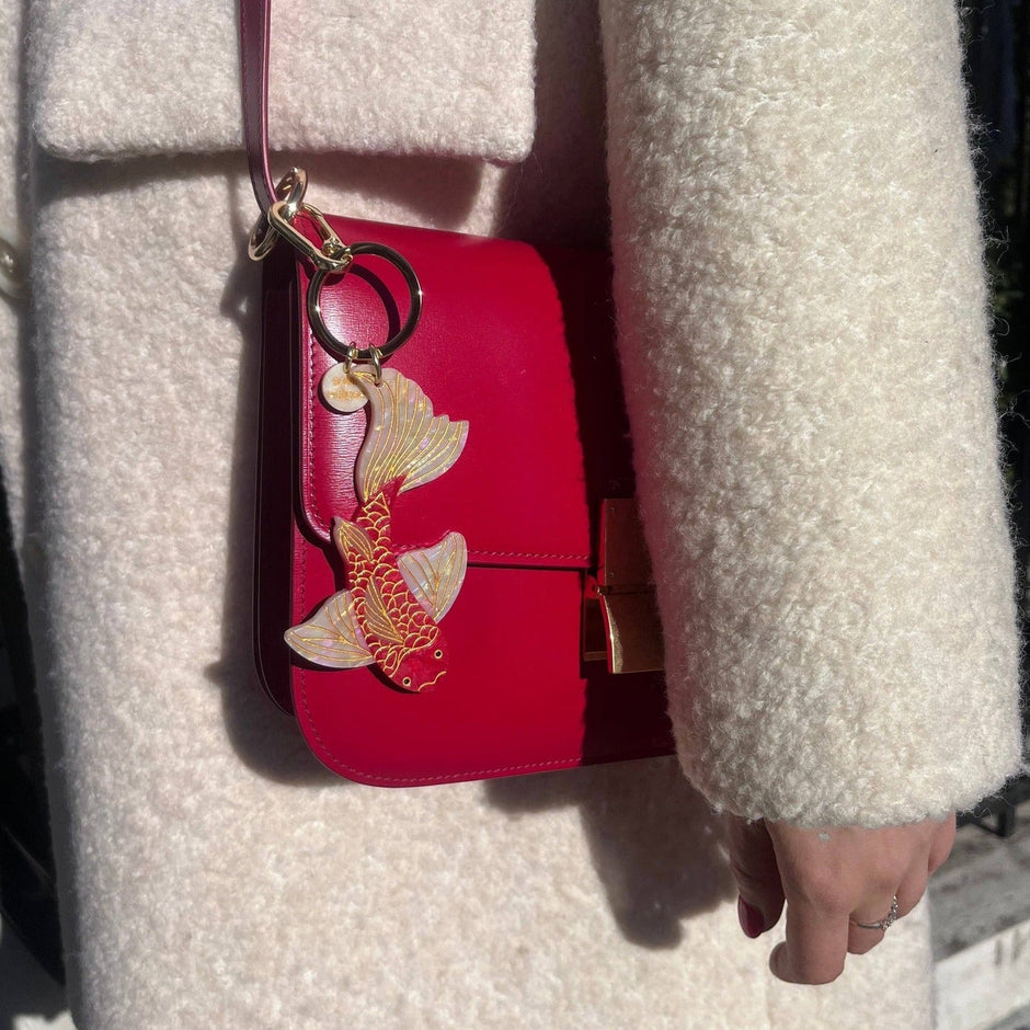 Red koi fish bag charm keychain held by model wearing cream cardigan in sunlight