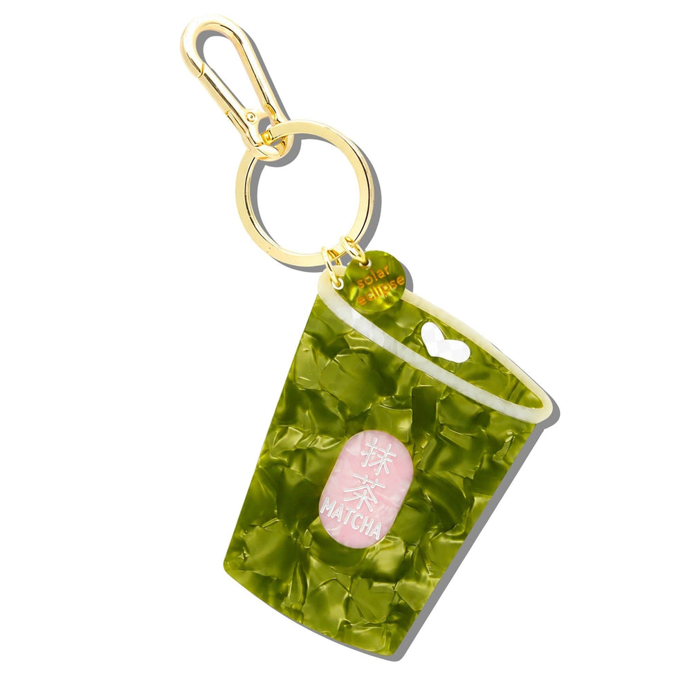 Green matcha bag charm keychain with pink label and gold hardware on white background