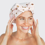 Woman wearing blush pink luxury shower cap with gold dots, smiling at camera
