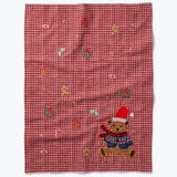 Red gingham tea towel with embroidered teddy bear wearing Santa hat and holiday decorations