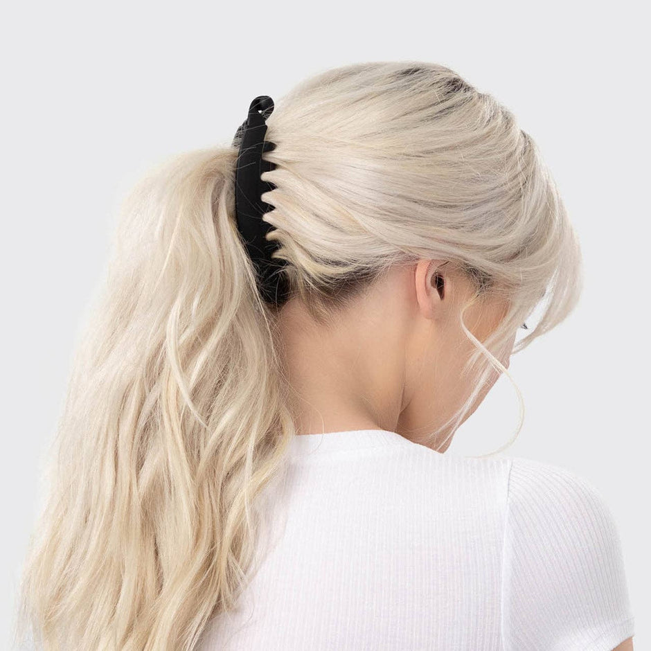 Black banana clip holding blonde wavy hair in ponytail on model wearing white top