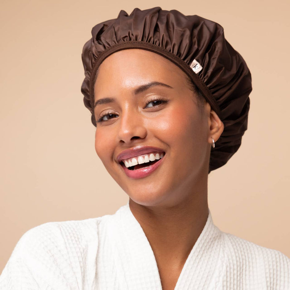 Woman wearing brown Kitsch shower cap, smiling against beige background