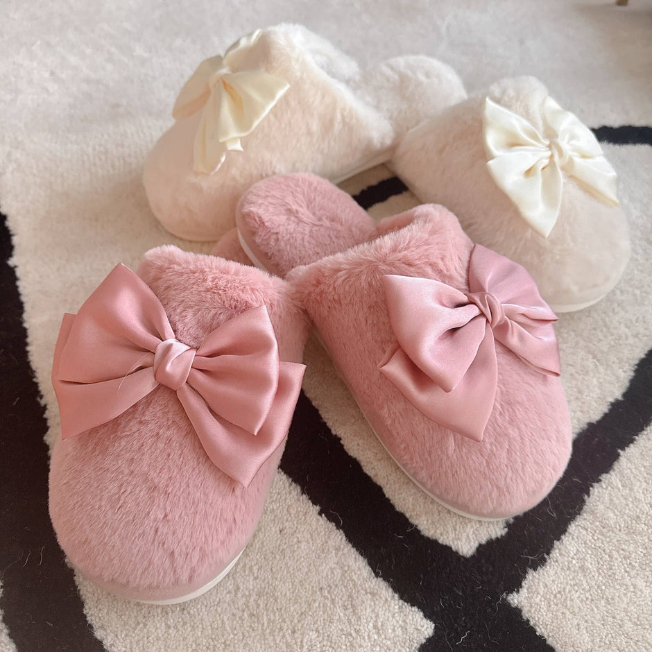 Pink and cream fur cozy lounge slippers with satin bows, displayed on patterned rug