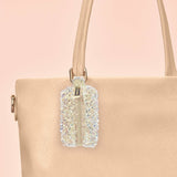 Champagne minimergency charm with crystallized embellishment hanging from beige tote bag