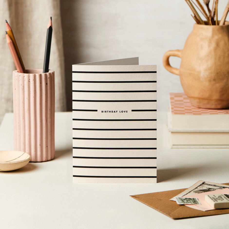 Katie Leamon Stripe Birthday Love greeting card displayed on white desk with stationery and flowers