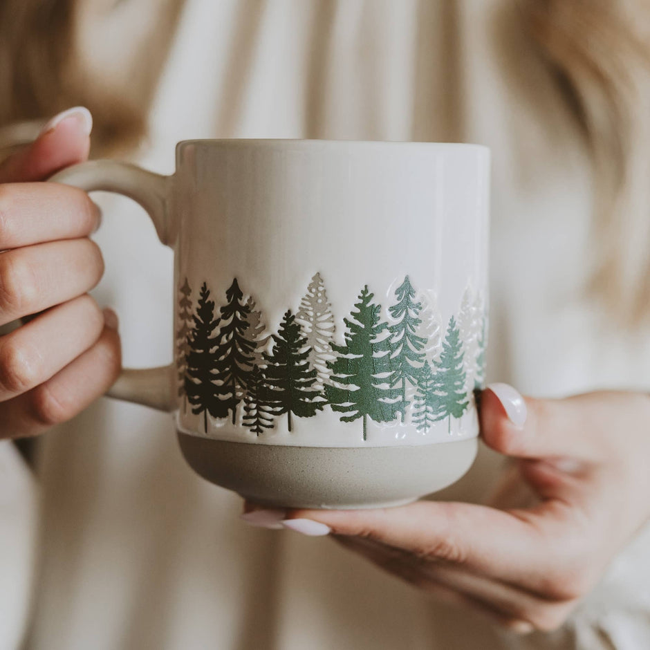 Person holding ceramic forest stoneware coffee mug with evergreen tree design