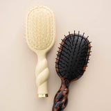 Tan mini detangler brush with twisted handle displayed next to tortoiseshell brush on neutral background