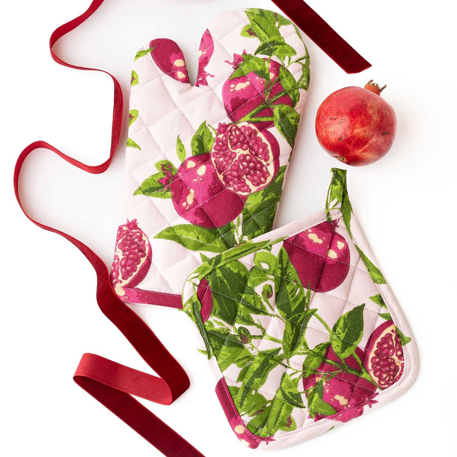 Pomegranate Grove oven mitt set with red ribbon and fresh pomegranate on white background