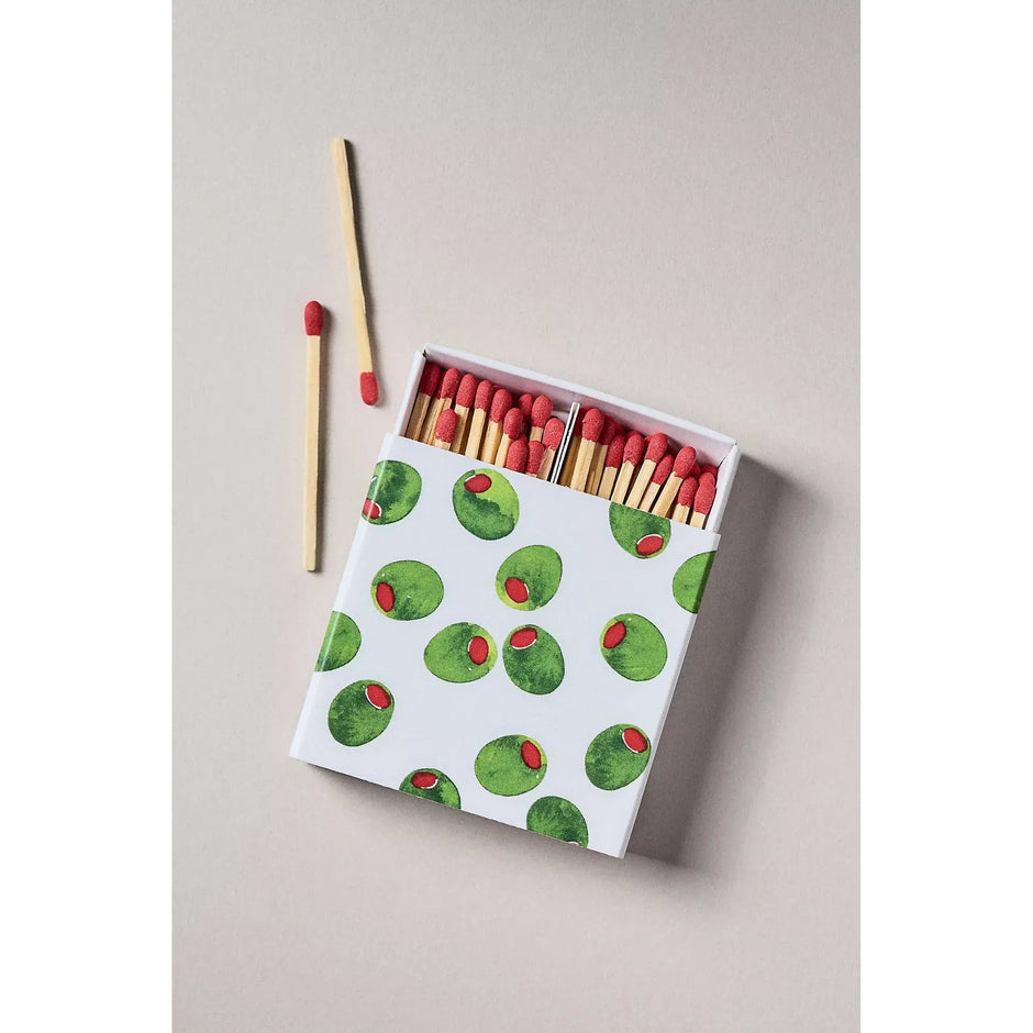 Olive-patterned celebration matches box with red match heads and wooden sticks on neutral background