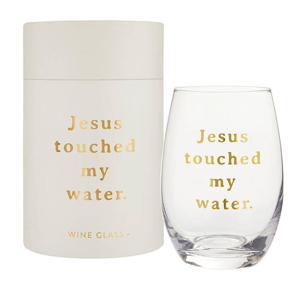 Stemless wine glass with 'Jesus touched my water' text in gold, shown with cream packaging box