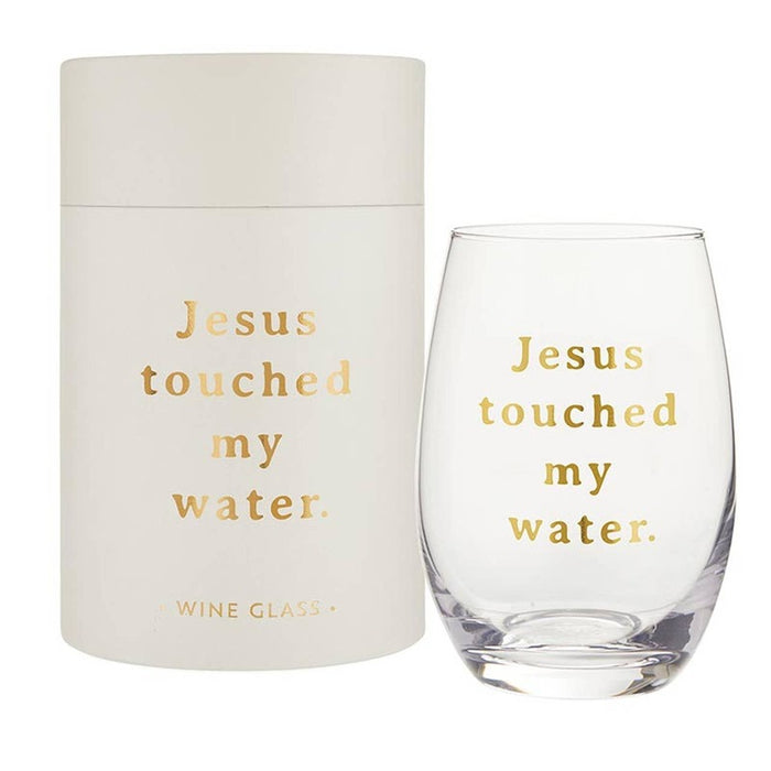 Stemless wine glass with 'Jesus touched my water' text in gold, shown with cream packaging box