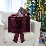 Red velvet tote bag with bow displayed on white chair in festive holiday setting with tree and ribbons