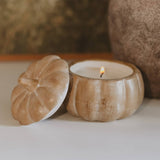 Pumpkin-shaped soy candle in wooden jar with lid, lit flame, autumn home decor