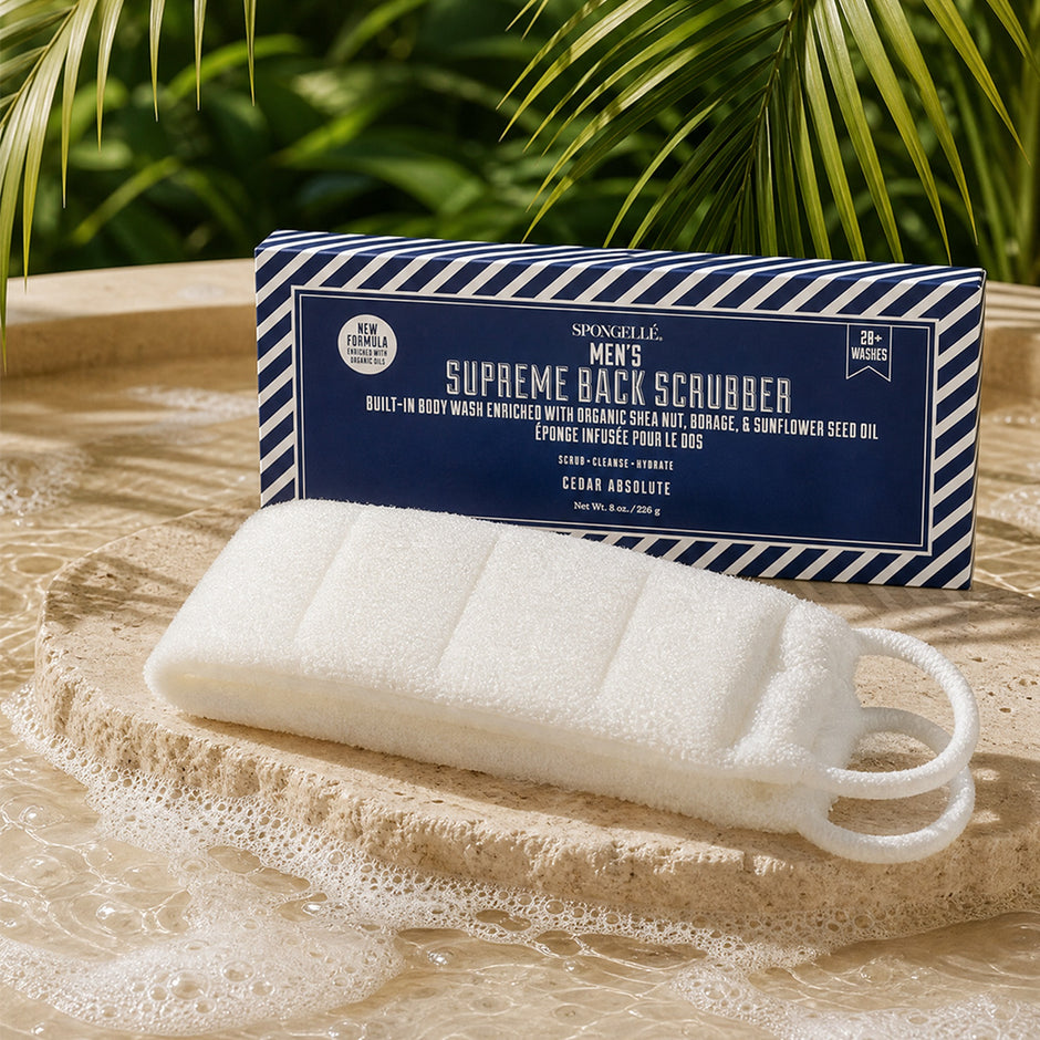 Spongellé Men's Supreme Back Scrubber displayed on sandy beach with ocean waves and palm fronds overhead