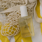 Baja Zen body glow oil displayed on yellow and white striped fabric with cream mesh accessories