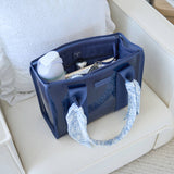 Navy tote organizer filled with essentials including keys, wallet, and cosmetics on a white cushioned surface