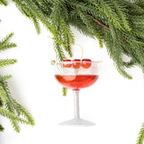 Dirty Shirley cocktail glass ornament with red liquid and cherry garnish surrounded by evergreen branches